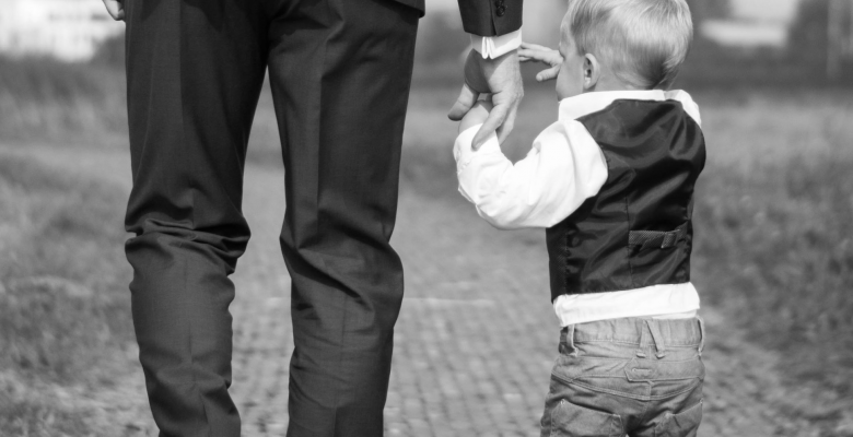 A father wearing a suit holds his toddler's hand. Photo by Sabine van Straaten