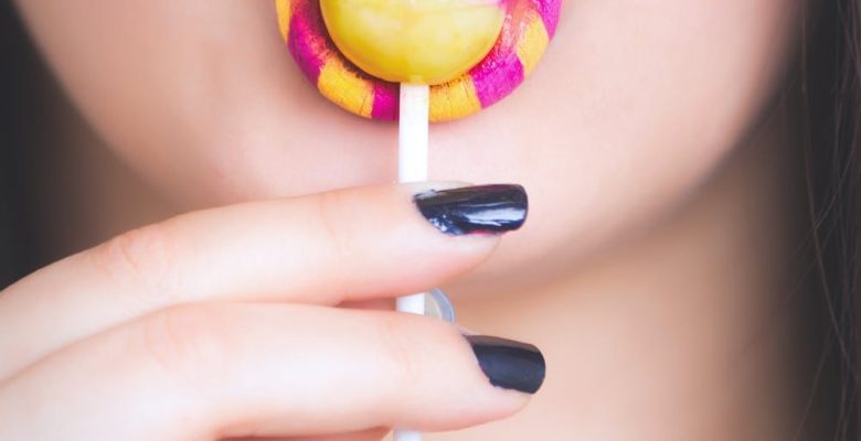 Sugar and Glyphosate: A Tale of Two Toxins. Photo of a woman with yellow and pink lipstick sucking a lolly. Courtesy of Oleg Magni via Pexels. | Jennifer Margulis