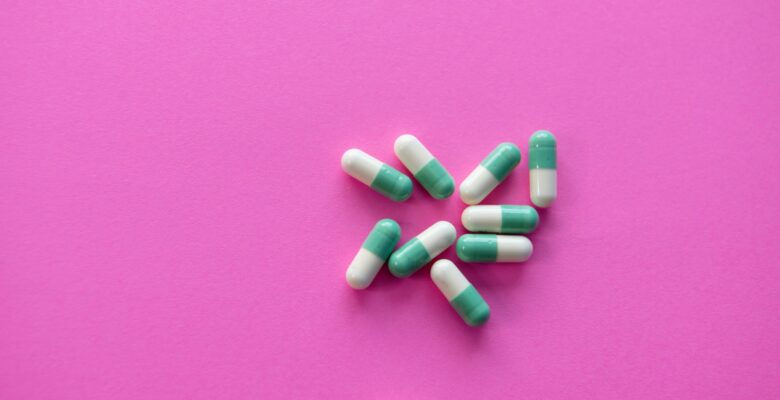Green and white pills on a pink background. COVID-19 and Tyenol, here's what you need to know. Photo courtesy of Christina Victoria Craft via Unsplash | Jennifer Margulis